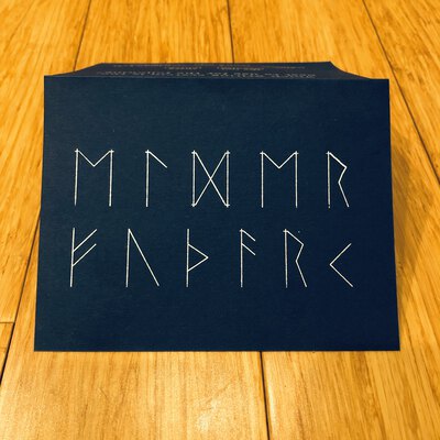 A folded card with the words Elder Futhark written in the Elder Futhark writing system.